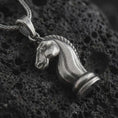 Load image into Gallery viewer, Sterling silver knight chess piece pendant necklace with an oxidized finish resting on textured volcanic rock, captured in a close-up premium studio composition.
