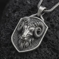 Load image into Gallery viewer, Sterling silver ram head shield pendant necklace with an oxidized finish resting on textured volcanic rock, captured in a close-up premium studio composition.