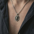 Load image into Gallery viewer, Ram head shield pendant necklace in oxidized sterling silver worn on the neck, styled in a dark lifestyle shot that emphasizes the bold Aries inspired design against the chest.