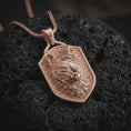 Load image into Gallery viewer, Wolf shield pendant necklace with a rose gold plated finish resting on textured black volcanic rock, shown in a premium close-up image with rich fur texture and a sharp shield outline.