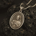 Load image into Gallery viewer, Bronze Saint Francis pendant necklace on textured volcanic rock, close-up studio shot highlighting the saint relief, lamb, birds, and antique silver contrast.