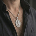 Load image into Gallery viewer, Polished silver Saint Michael spinning pendant necklace worn on the chest, masculine lifestyle shot highlighting the archangel wings, sword, shield detail, and bright silver finish.