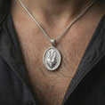 Load image into Gallery viewer, Polished silver Sacred Heart pendant necklace worn on the chest, masculine lifestyle shot highlighting the flaming heart relief, cross detail, and bright silver finish.