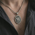Load image into Gallery viewer, Oxidized Saint George pendant necklace worn on the chest, close-up lifestyle jewelry photo showing the dragon slayer medallion on a spiga chain with dark clothing.