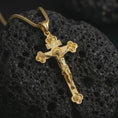 Load image into Gallery viewer, Gold plated crucifix pendant necklace presented on dark volcanic stone, photographed in a luxury close-up composition showcasing the ornate Christian cross silhouette and symbolic craftsmanship.