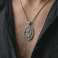 Load image into Gallery viewer, Oxidized Madonna and Child pendant necklace worn on the neck, styled in a dark lifestyle photograph that presents the oval Catholic medal as a meaningful symbol of faith, love, and protection.