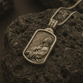 Load image into Gallery viewer, Bronze Jesus prayer dog tag pendant necklace on textured volcanic rock, close-up studio shot highlighting the side-profile Christ relief, halo, prayer pose, and antique silver contrast.