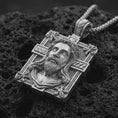 Load image into Gallery viewer, A Jesus crucifix pendant in a polished silver finish resting on porous volcanic rock in a premium macro studio shot.
