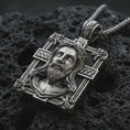 Load image into Gallery viewer, A Jesus crucifix pendant in an oxidized finish resting on porous volcanic rock in a premium macro studio shot.