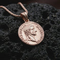 Load image into Gallery viewer, Rose gold plated Tiberius coin pendant necklace presented on textured volcanic stone, showcasing the round Roman coin silhouette and emperor bust in a refined macro studio shot.