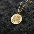 Load image into Gallery viewer, Gold plated heraldic eagle coin pendant necklace photographed on porous black volcanic stone, emphasizing the regal emblem, round medallion silhouette, and symbolic laurel accents in a luxury jewelry composition.