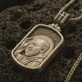 Load image into Gallery viewer, Bronze Saint Padre Pio dog tag pendant necklace on textured volcanic rock, close-up studio shot highlighting the saint profile, blessing gesture, halo, and antique silver contrast.