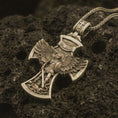 Load image into Gallery viewer, Bronze Saint Michael cross pendant necklace on textured volcanic rock, close-up studio shot highlighting the archangel wings, sword, shield, demon detail, and antique silver contrast.