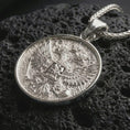 Load image into Gallery viewer, Polished silver double headed eagle pendant necklace displayed on dark volcanic rock, shown in a premium close-up image that highlights the imperial bird emblem, crown detail, and ornate relief texture.