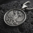 Load image into Gallery viewer, Oxidized double headed eagle pendant necklace resting on black volcanic stone, featuring a detailed heraldic eagle crest with spread wings and central shield in a macro product photograph.