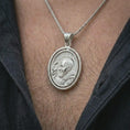 Load image into Gallery viewer, Polished silver Saint Padre Pio spinning pendant necklace worn on the neck, shown in a clean model shot with the oval saint portrait centered for a timeless devotional look.