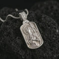 Load image into Gallery viewer, Polished silver Joan of Arc dog tag pendant necklace displayed on dark volcanic rock, shown in a premium close-up image that highlights the armored saint relief, spear backdrop, and rounded rectangular frame.