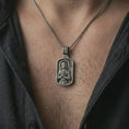 Load image into Gallery viewer, Oxidized Joan of Arc dog tag pendant necklace worn on the neck, styled in a dark lifestyle image that presents the saint warrior medal as a symbol of faith, courage, and spiritual strength.