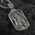Load image into Gallery viewer, Oxidized Saint Barbara pendant necklace on textured volcanic rock, close-up studio shot highlighting the saint relief, cross, tower detail, and dark antique silver contrast.
