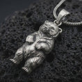 Load image into Gallery viewer, Oxidized baby bear pendant necklace on textured volcanic rock, close-up studio shot highlighting the cute bear cub charm, rounded paws, detailed fur, and antique silver contrast.