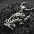 Load image into Gallery viewer, Oxidized chameleon pendant necklace on textured volcanic rock, close-up studio shot highlighting the lizard body, curled tail, branch detail, leaves, and antique silver contrast.
