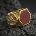 Load image into Gallery viewer, A red onyx signet ring in a gold plated finish resting on porous volcanic rock in a premium macro studio shot.