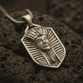 Load image into Gallery viewer, Bronze pharaoh shield pendant necklace on textured volcanic rock, close-up studio shot highlighting the Egyptian king portrait, royal headdress, shield frame, and antique silver contrast.