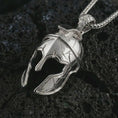 Load image into Gallery viewer, Polished silver Spartan helmet pendant necklace on textured volcanic rock, centered macro jewelry photo with detailed ancient warrior helmet sculpting and bright silver highlights.