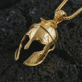 Load image into Gallery viewer, Gold plated Spartan helmet pendant necklace on textured volcanic rock, premium close-up studio composition emphasizing the battle helmet shape, cracked armor texture, and heroic warrior symbolism.
