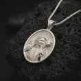 Load image into Gallery viewer, Polished silver Good Shepherd Jesus pendant necklace on textured volcanic rock, centered macro jewelry photo with detailed religious relief and bright silver highlights.