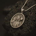 Load image into Gallery viewer, Bronze Good Shepherd Jesus pendant necklace on textured volcanic rock, close-up studio shot highlighting the shepherd relief, lamb detail, and antique silver contrast.