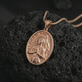 Load image into Gallery viewer, Rose gold plated Saint Joan of Arc pendant necklace on textured volcanic rock, detailed macro product shot with soft warm reflections and devotional saint symbolism.