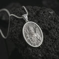 Load image into Gallery viewer, Polished silver Saint Patrick pendant necklace on textured volcanic rock, centered macro jewelry photo with detailed Irish patron saint engraving and bright silver highlights.