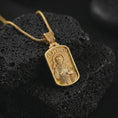 Load image into Gallery viewer, Gold plated Saint Francis pendant necklace on textured volcanic rock, premium close-up studio composition emphasizing the saint figure, bird, and wolf symbolism.
