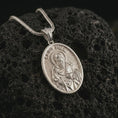 Load image into Gallery viewer, Polished silver Saint Paul pendant necklace on textured volcanic rock, centered macro jewelry photo with detailed Catholic medal engraving and bright silver highlights.