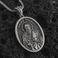 Load image into Gallery viewer, Oxidized Saint Paul pendant necklace on textured volcanic rock, close-up studio shot highlighting the apostle relief, sword, book detail, and antique silver contrast.