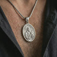 Load image into Gallery viewer, Polished silver Saint Andrew pendant necklace worn on the chest, masculine lifestyle shot highlighting the apostle relief, cross, book detail, and bright silver finish.