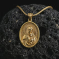 Load image into Gallery viewer, Gold plated Virgin Mary and baby Jesus pendant necklace on textured volcanic rock, premium close-up studio composition emphasizing the Madonna and child design with sacred halo details.