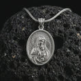 Load image into Gallery viewer, Polished silver Virgin Mary and baby Jesus pendant necklace on textured volcanic rock, centered macro jewelry photo with detailed devotional relief and bright silver highlights.