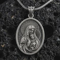 Load image into Gallery viewer, Oxidized Virgin Mary and baby Jesus pendant necklace on textured volcanic rock, close-up studio shot highlighting the mother and child relief, halo, star border, and antique silver contrast.