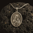 Load image into Gallery viewer, Bronze Virgin Mary and baby Jesus pendant necklace on textured volcanic rock, close-up studio shot highlighting the mother and child relief, halo, star border, and antique silver contrast.