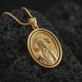Load image into Gallery viewer, Gold plated spinning Good Shepherd pendant necklace on textured volcanic rock, premium close-up studio composition emphasizing the Jesus figure, lamb detail, and rotating frame design.