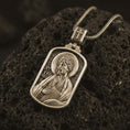 Load image into Gallery viewer, Bronze Saint James the Apostle pendant necklace on textured volcanic rock, close-up studio shot highlighting the apostle relief, halo, book detail, and antique silver contrast.