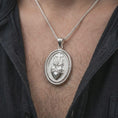 Load image into Gallery viewer, Polished silver Sacred Heart pendant necklace worn on the chest, masculine lifestyle shot highlighting the flaming heart relief, cross detail, and bright silver finish.