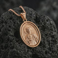 Load image into Gallery viewer, Rose gold plated Saint Jude pendant necklace on textured volcanic rock, detailed macro product shot with soft warm reflections and devotional Saint Jude design.