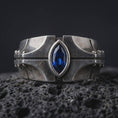 Load image into Gallery viewer, A sterling silver ring with an oxidized finish and marquise blue stone displayed on textured volcanic rock in a premium macro shot.