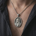 Load image into Gallery viewer, Oxidized Jesus Christ Good Shepherd pendant necklace worn on the chest, close-up lifestyle jewelry photo showing the Christian medallion on a spiga chain with dark clothing.