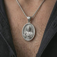 Load image into Gallery viewer, Polished silver Saint Francis pendant necklace worn on the chest, masculine lifestyle shot highlighting the saint relief, lamb, bird detail, and bright silver finish.