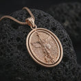 Load image into Gallery viewer, Rose gold plated Saint Michael spinning pendant necklace on textured volcanic rock, detailed macro product shot with soft warm reflections and protective archangel symbolism.