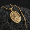 Load image into Gallery viewer, Gold plated Saint James the Apostle pendant necklace on textured volcanic rock, premium close-up studio composition emphasizing the apostle figure, halo, and sacred book symbolism.